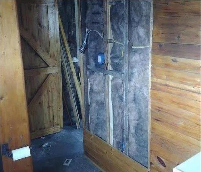 Paneling on a wooden wall is removed to reveal smoke and fire damage.